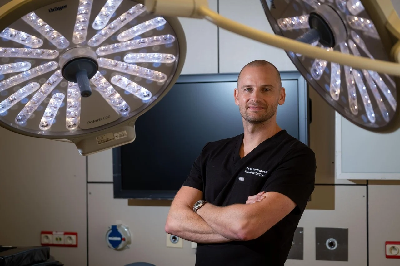Dr. Maarten Van Genechten in chirurgisch tenue die poseert in een operatiekamer met gekruiste armen.