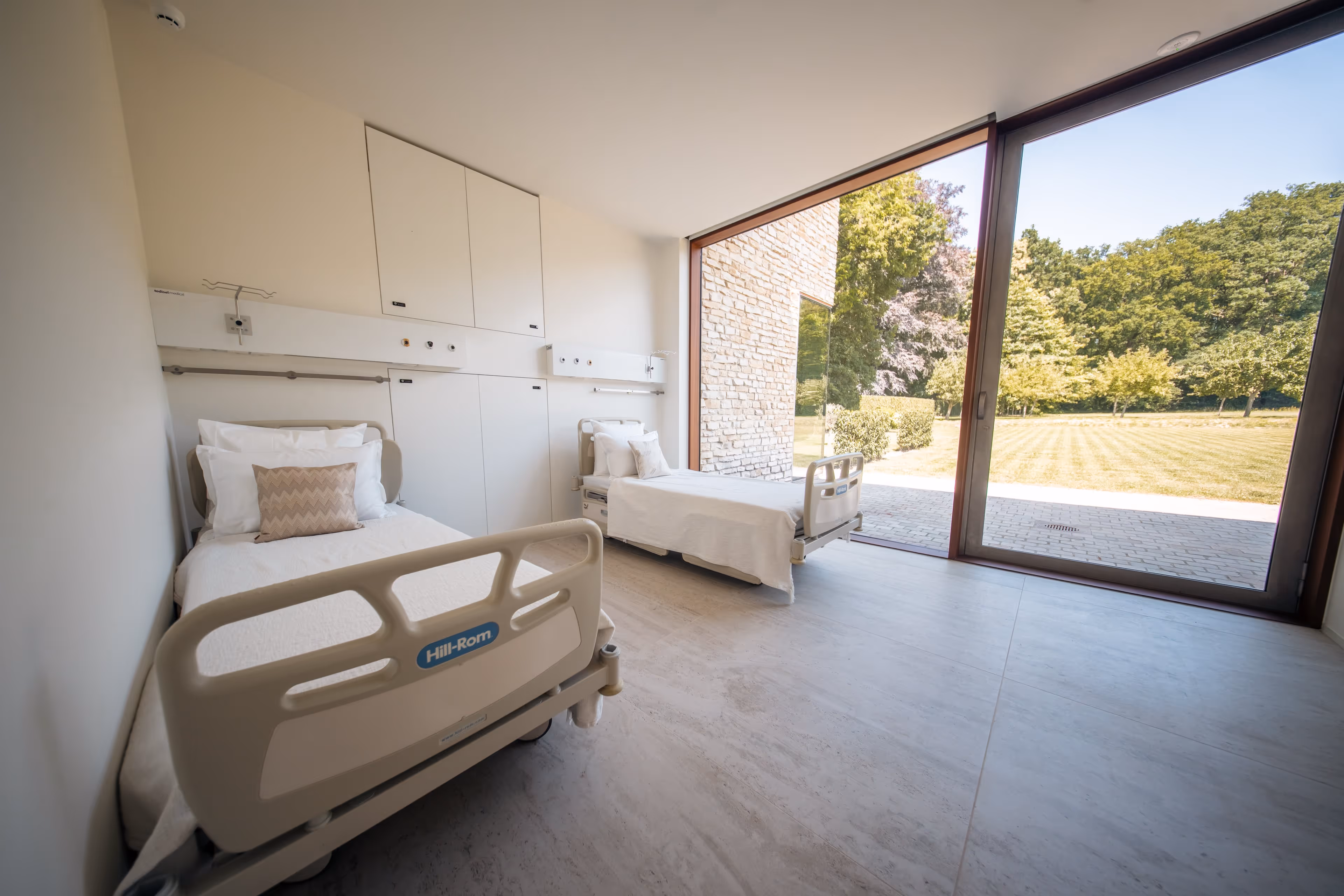 Wide shot of the recovery room with two beds and view of a green garden.
