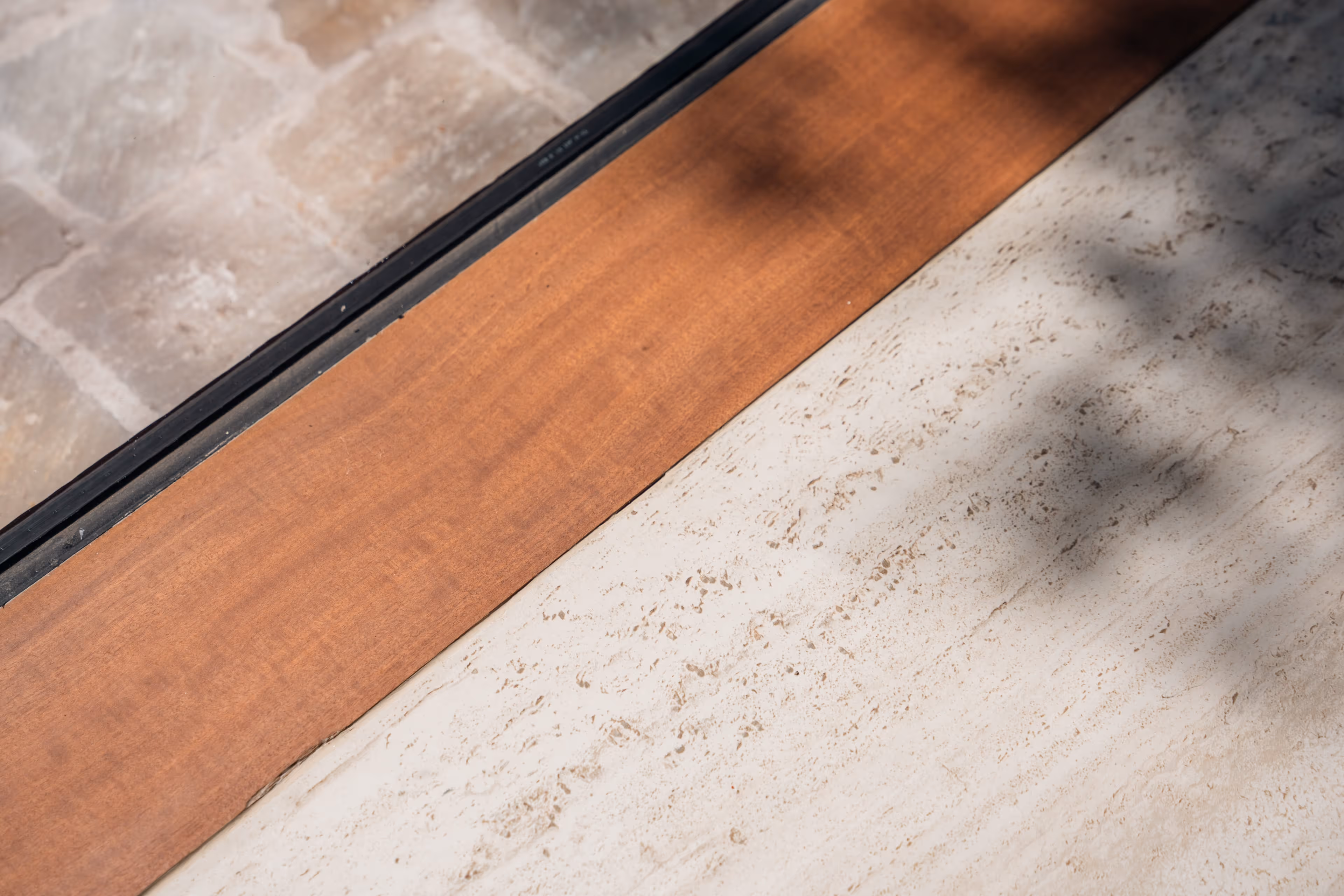 Detail van drie aansluitende vloerafwerkingen: natuursteen, hout en beige tegel.