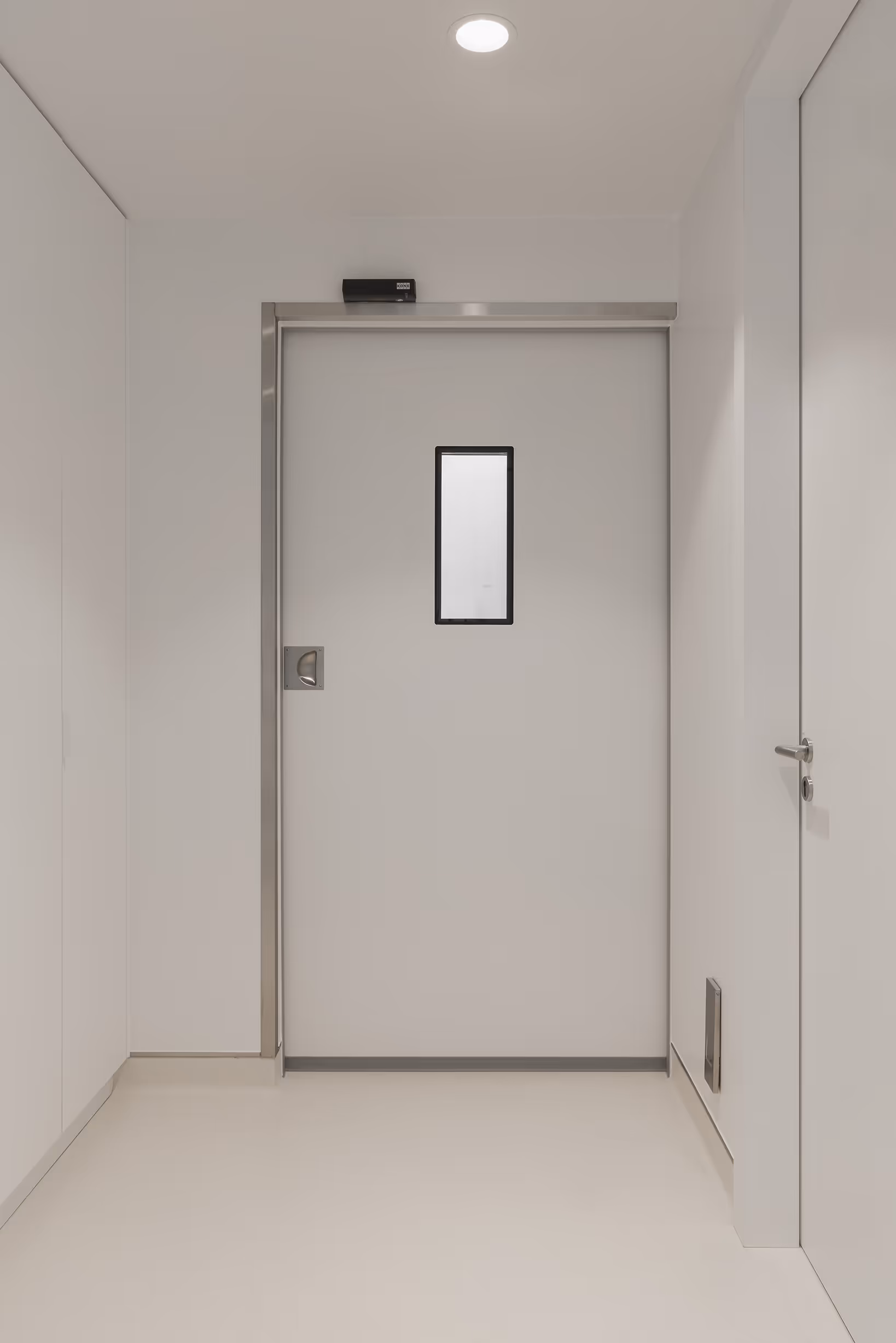 Een minimalistische witte binnendeur met een klein rechthoekig raam, omringd door een strakke, witte ruimte met ingebouwde verlichting.
