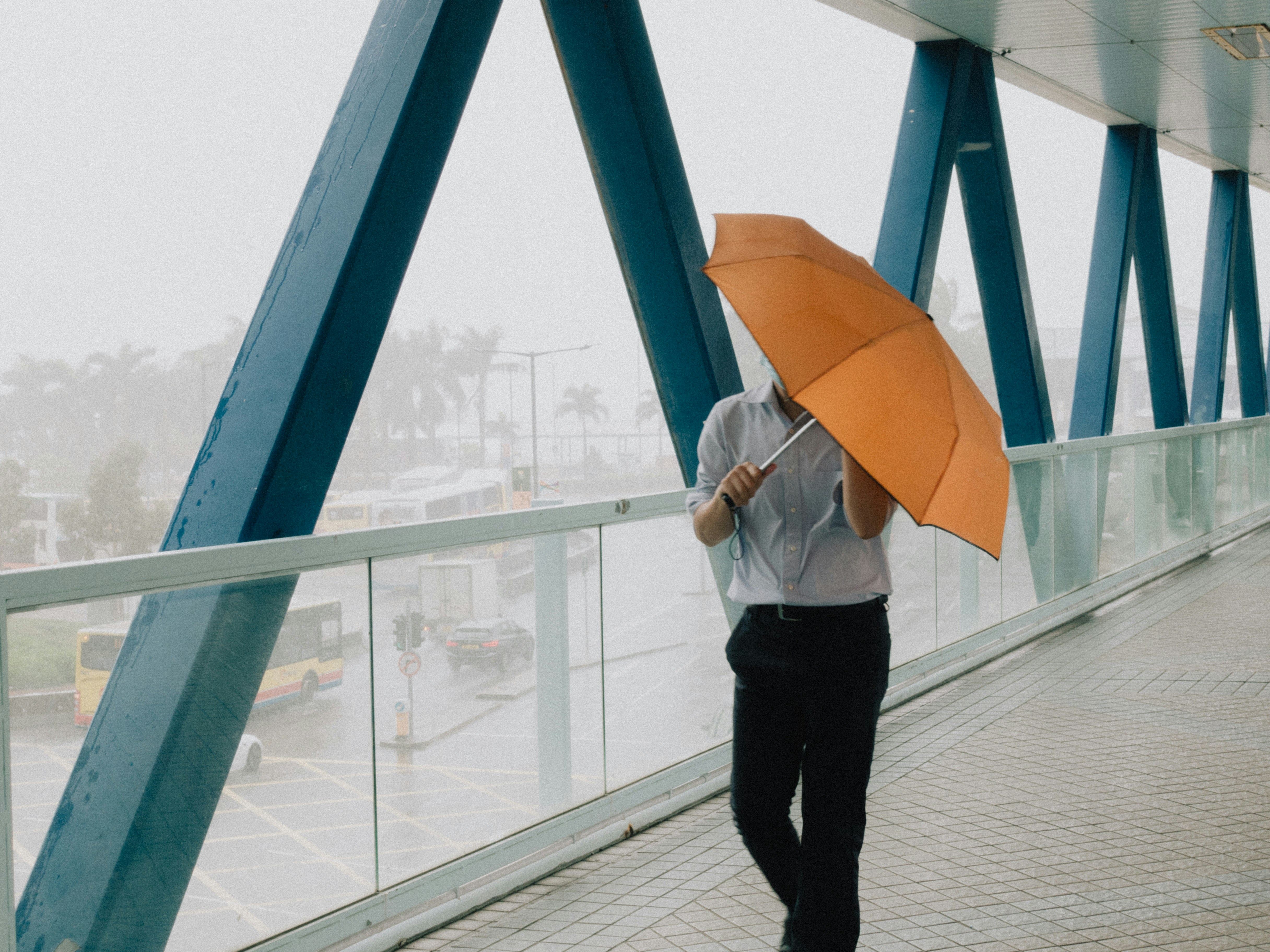 A guy in suit holding an umbrella during a typhoon day on a pedestrian footbridge in Hong Kong