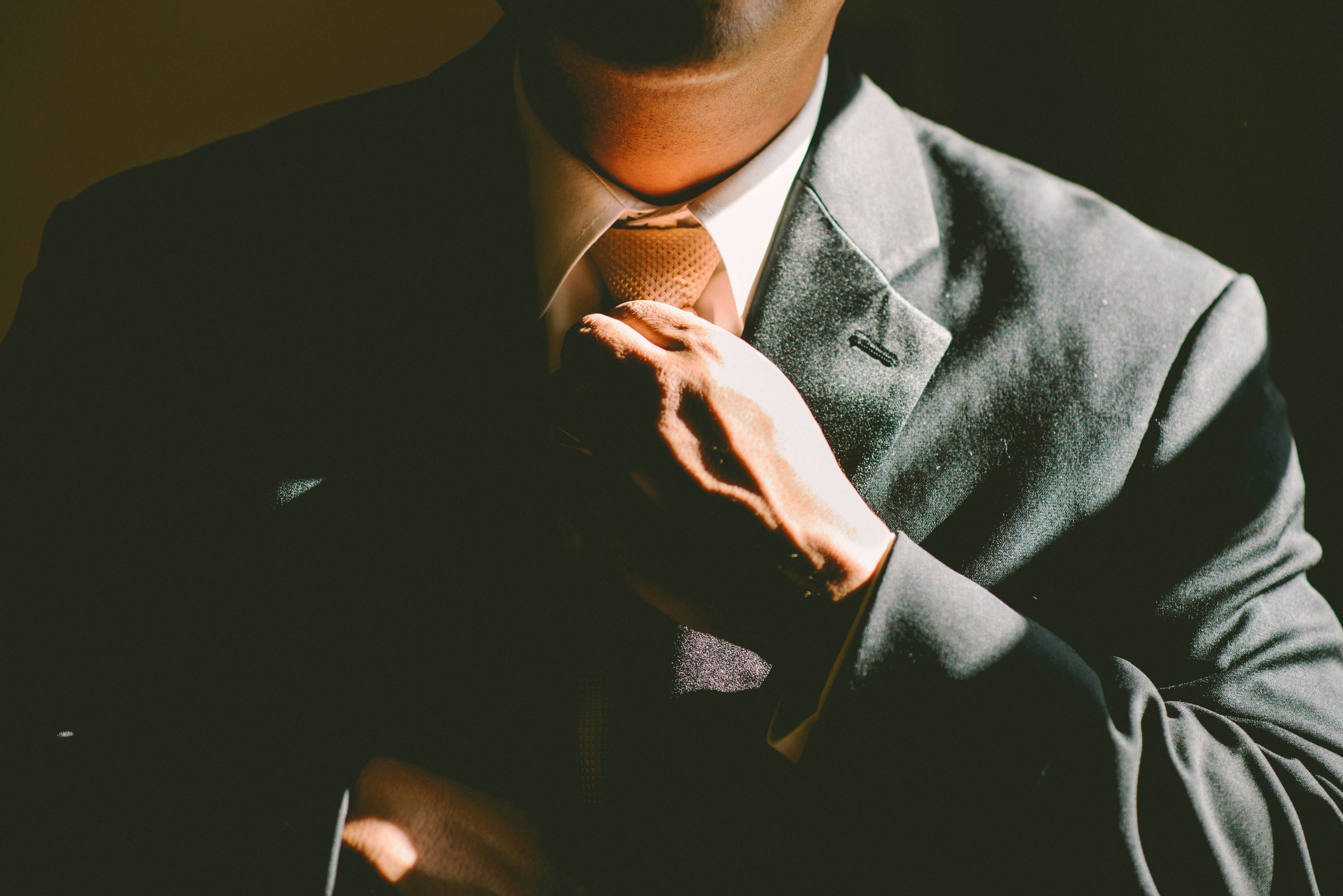 A guy in suit tidying up his tie with his left hand
