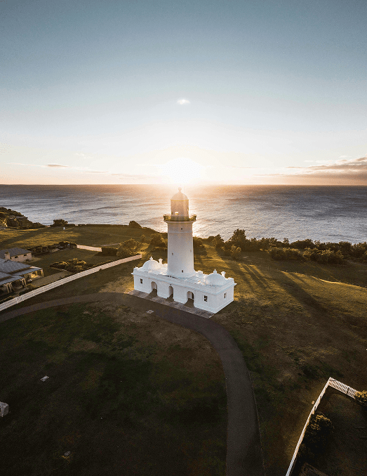 White lighthouse on grassy cliff overlooking ocean at sunset.