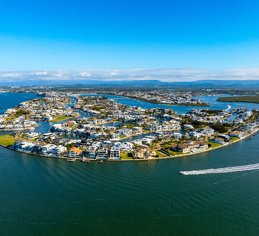 Aerial view of a coastal residential area with modern houses surrounded by water channels and a speedboat moving in the water.