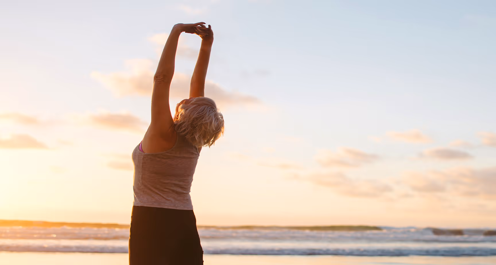 Woman stretching her arms overhead on the beach at sunrise or sunset.