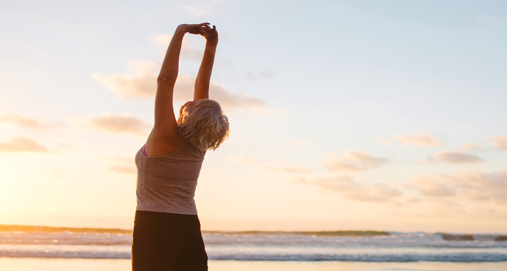 Woman stretching her arms overhead on the beach at sunrise or sunset.