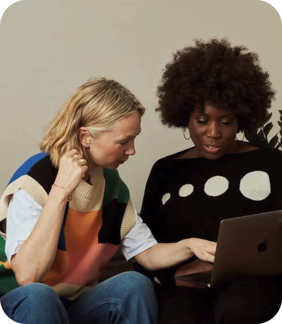Two women sitting on a couch looking at a laptop.