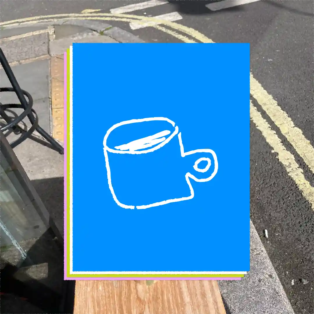 Stack of colorful cards on a wooden bench with a white line-drawn coffee cup on the top blue card, outdoors near a street curb.