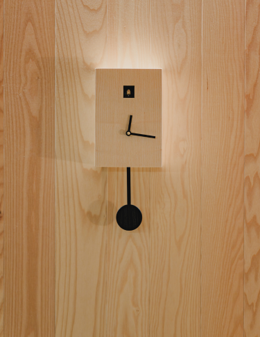Horloge murale design minimaliste sur un mur en bois naturel, détail décoratif épuré illustrant l'art de vivre et le confort moderne au sein d'une suite itinérante SNUUG en Suisse.