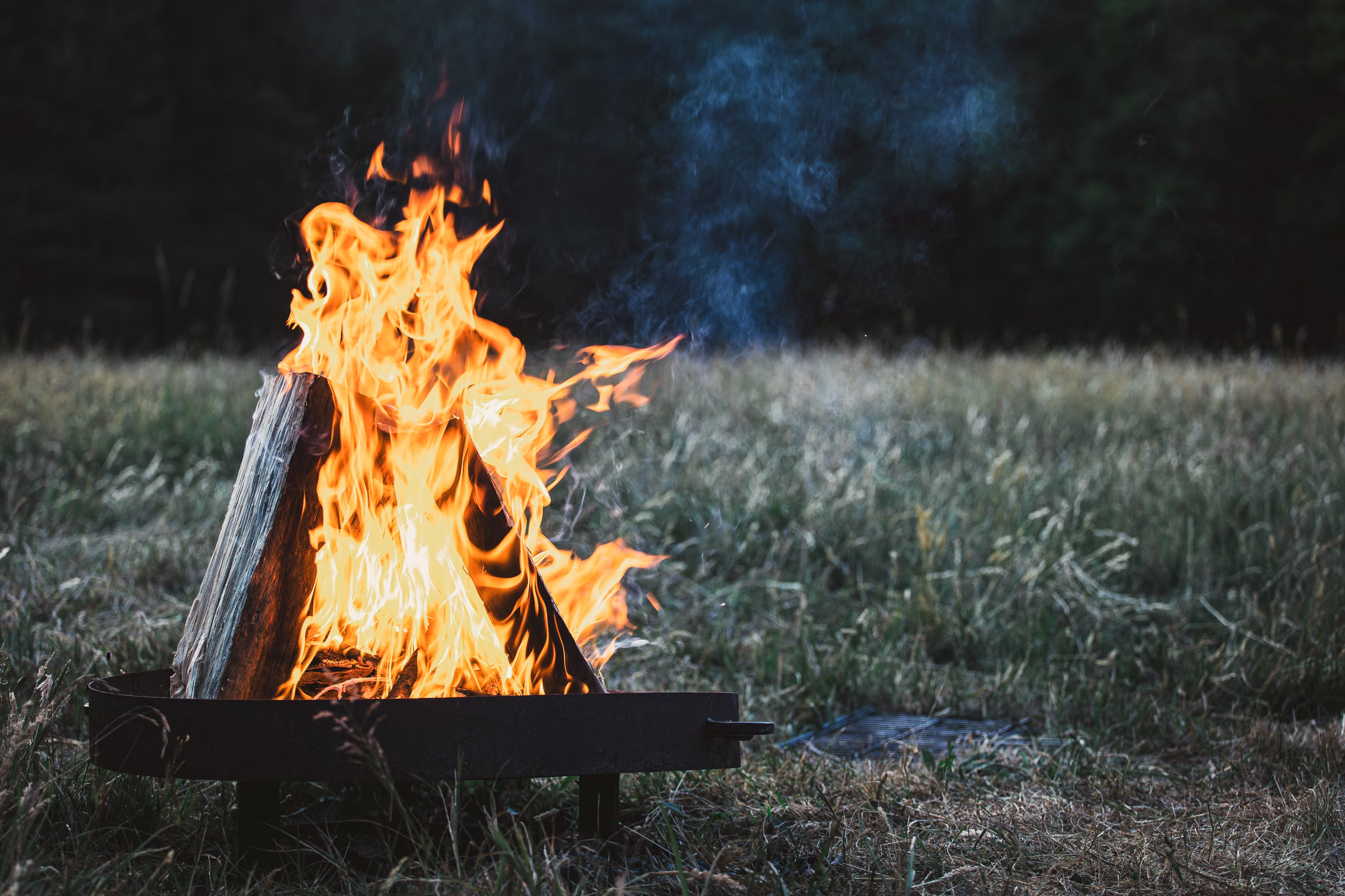 A crackling campfire in a Swiss meadow at dusk, embodying the comfort and exclusive experience of a pop-up 4-star hotel in the heart of nature.