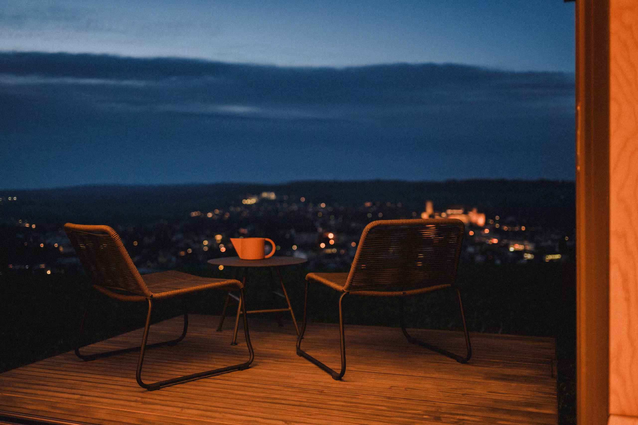 Terrasse en bois SNUUG avec deux chaises face à un paysage nocturne illuminé en Suisse, parenthèse exclusive sous les étoiles.