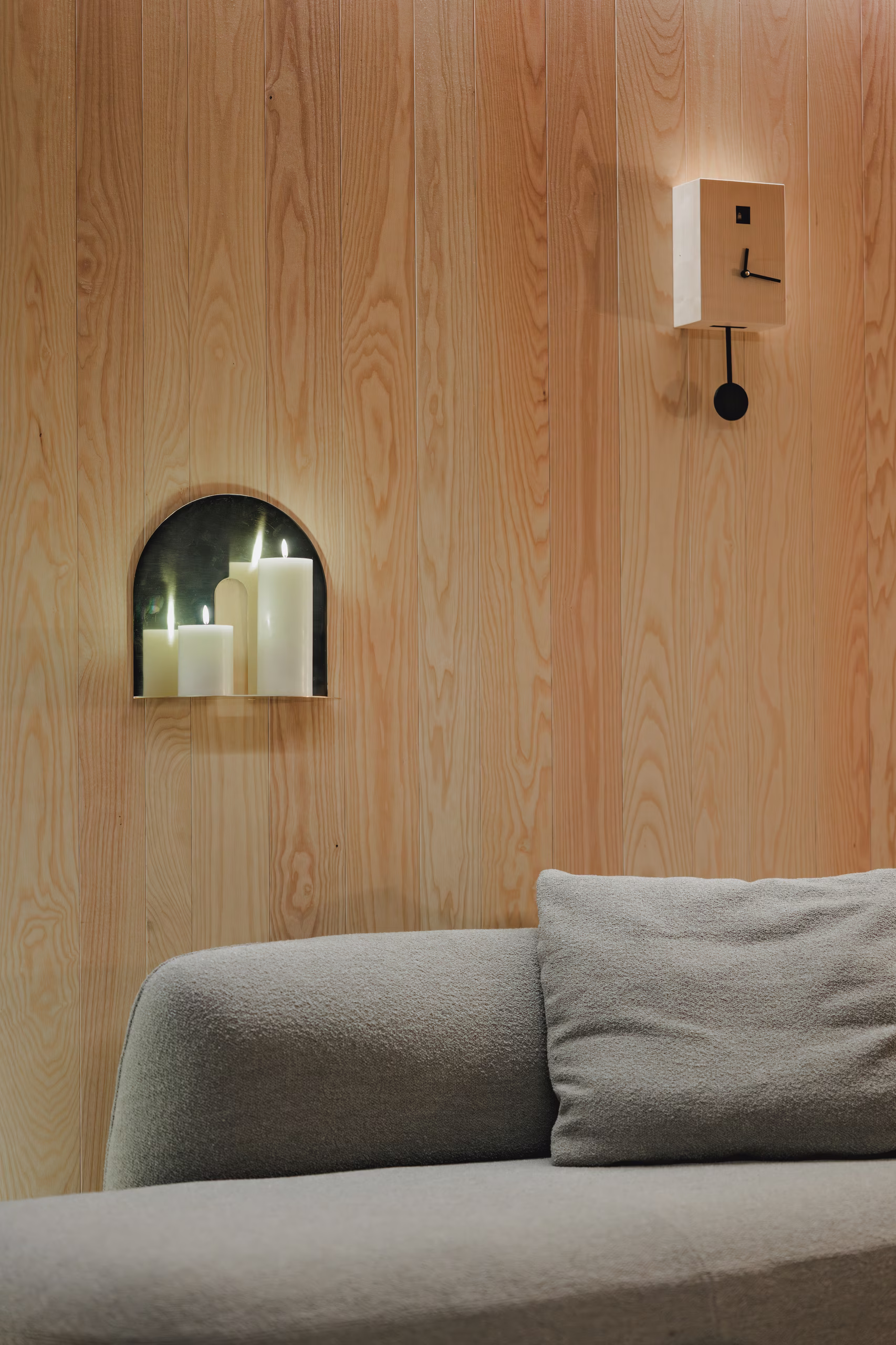 Atmosfera avvolgente con candele e orologio di design su una parete in legno naturale, il comfort poetico di un soggiorno SNUUG, hotel eco-responsabile itinerante.