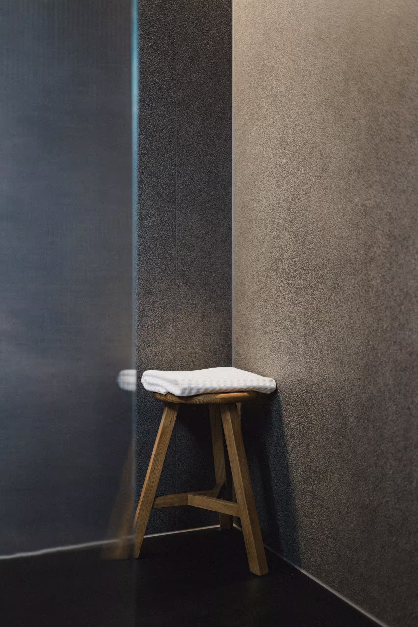 Tabouret artisanal en bois brut dans une salle de bain moderne aux tons sombres, détail du design raffiné des hébergements durables SNUUG.