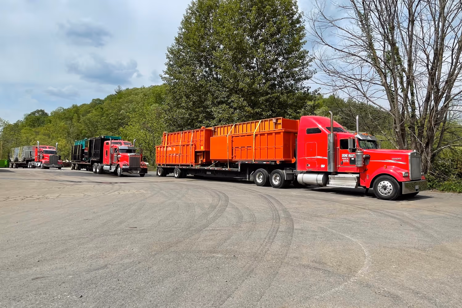 Three red semis with roll-off containers on the trailers
