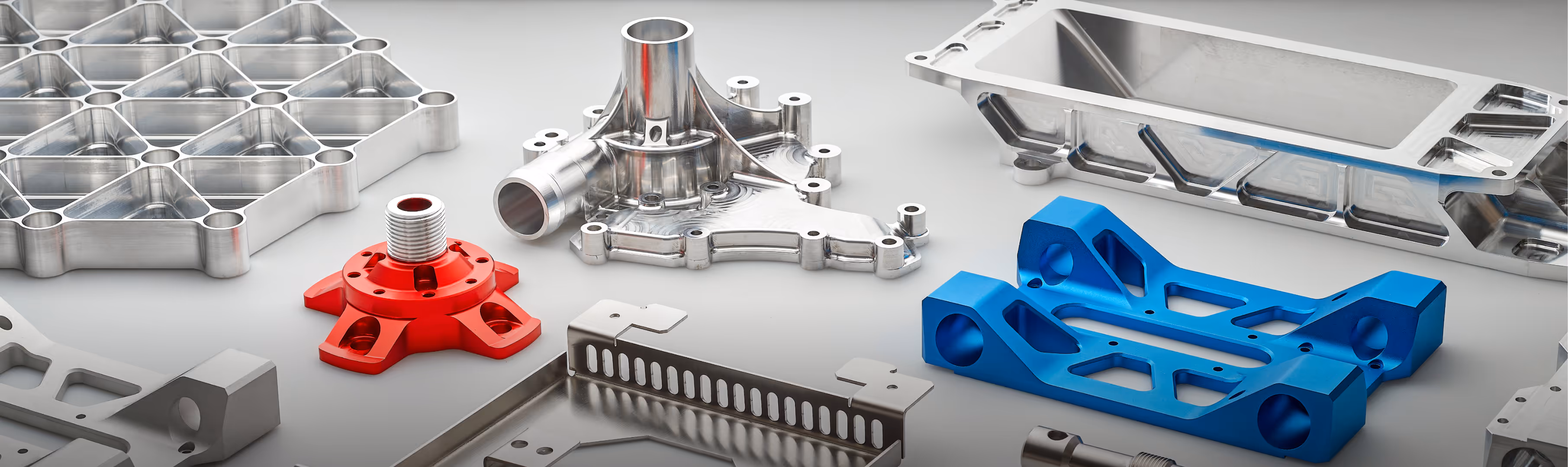 Various precision-machined metal parts including silver, red, and blue components arranged on a light surface.