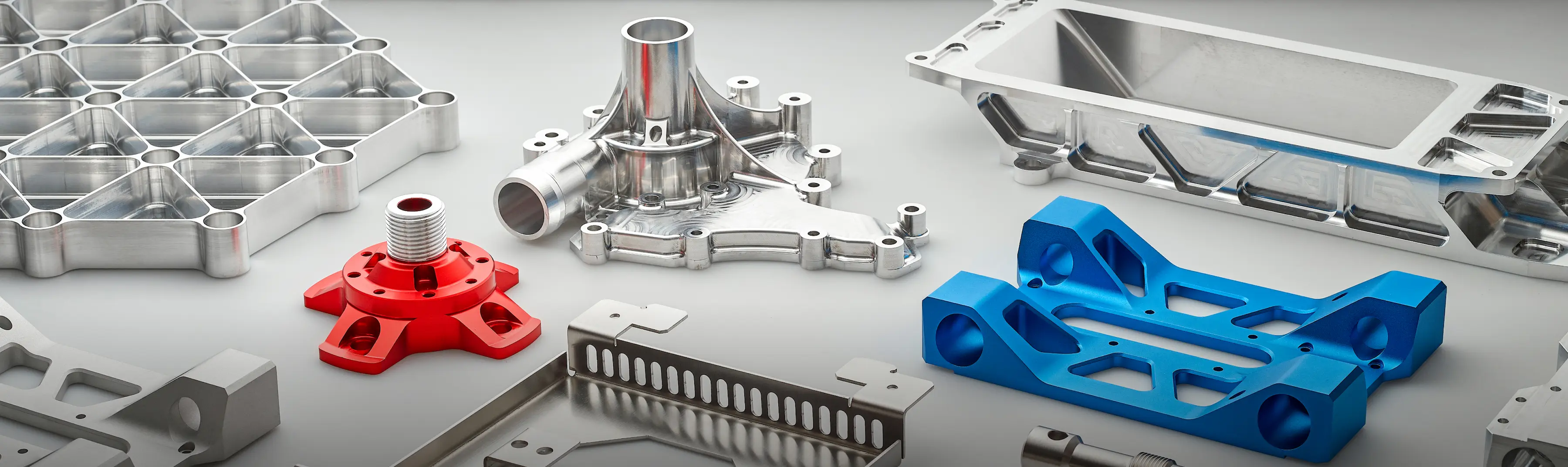 Various precision CNC machined metal parts including silver, red, and blue components with complex shapes on a gray surface.
