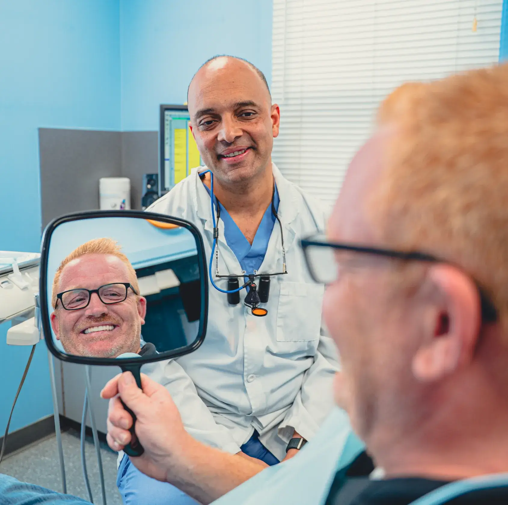 Patient looking dental treatment results in the mirror, with Dr. Cherian in the background.