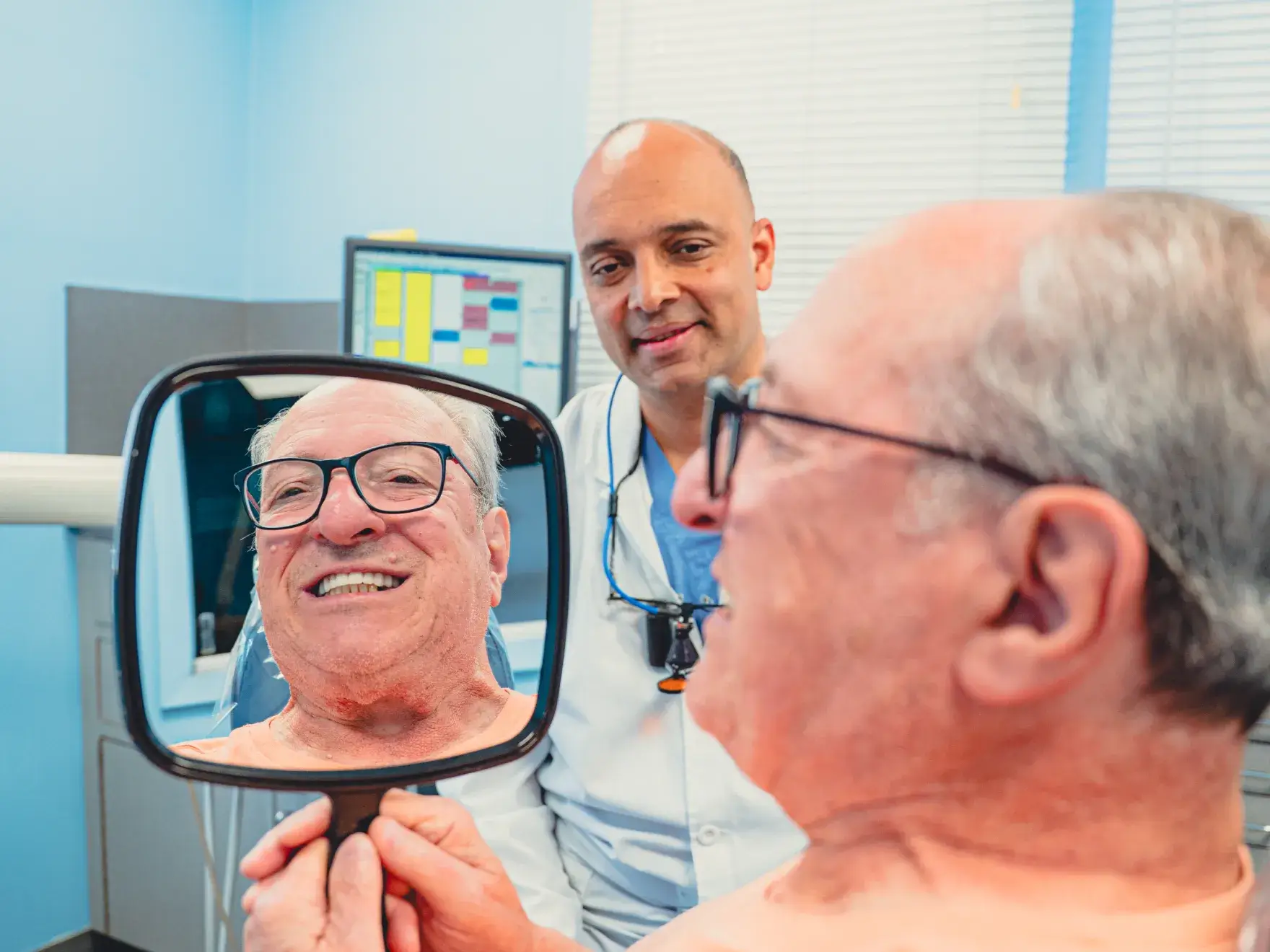 Patient looking dental treatment results in the mirror, with Dr. Cherian in the background.