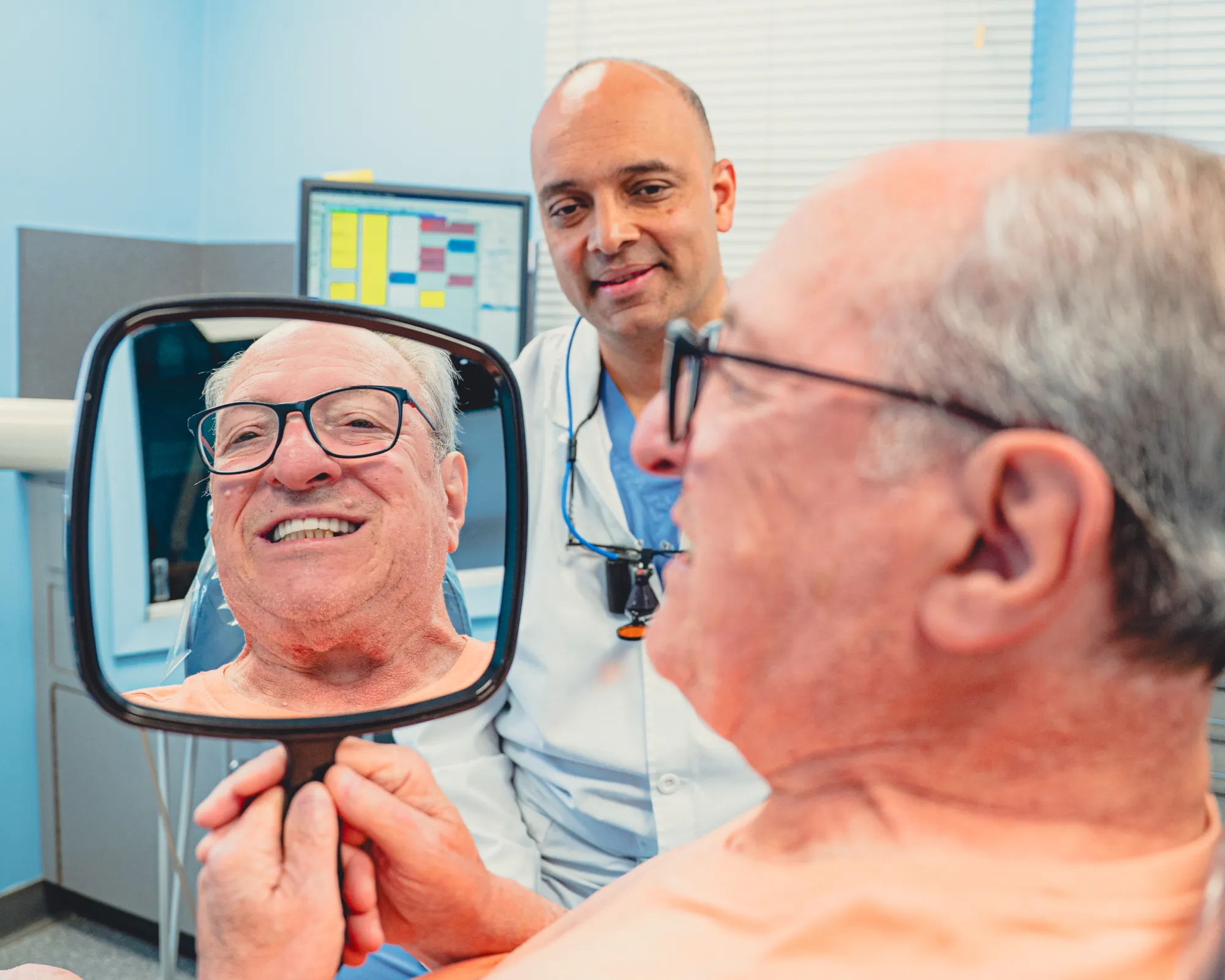 Patient looking dental treatment results in the mirror, with Dr. Cherian in the background.