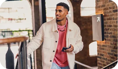 Young man in a light jacket holding a phone and walking up stairs in a modern building.
