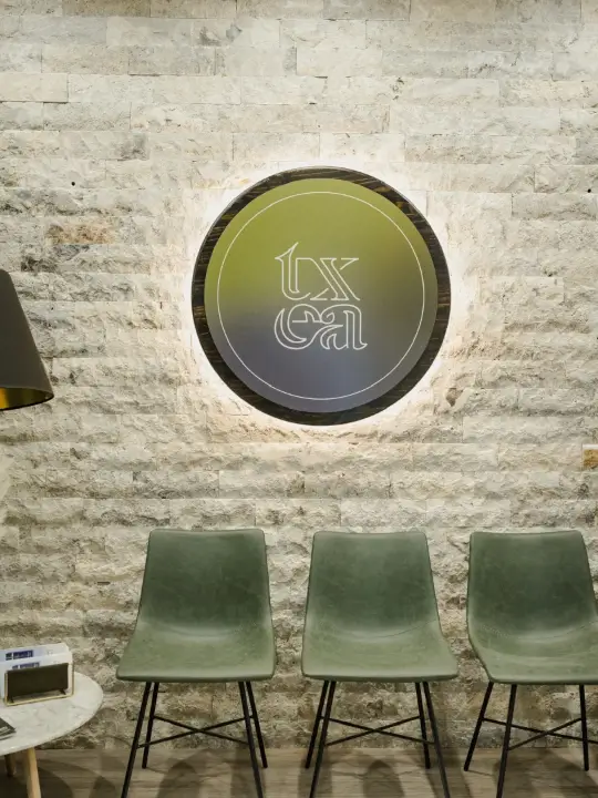 Three green chairs against a stone wall under a round illuminated sign with stylized text.