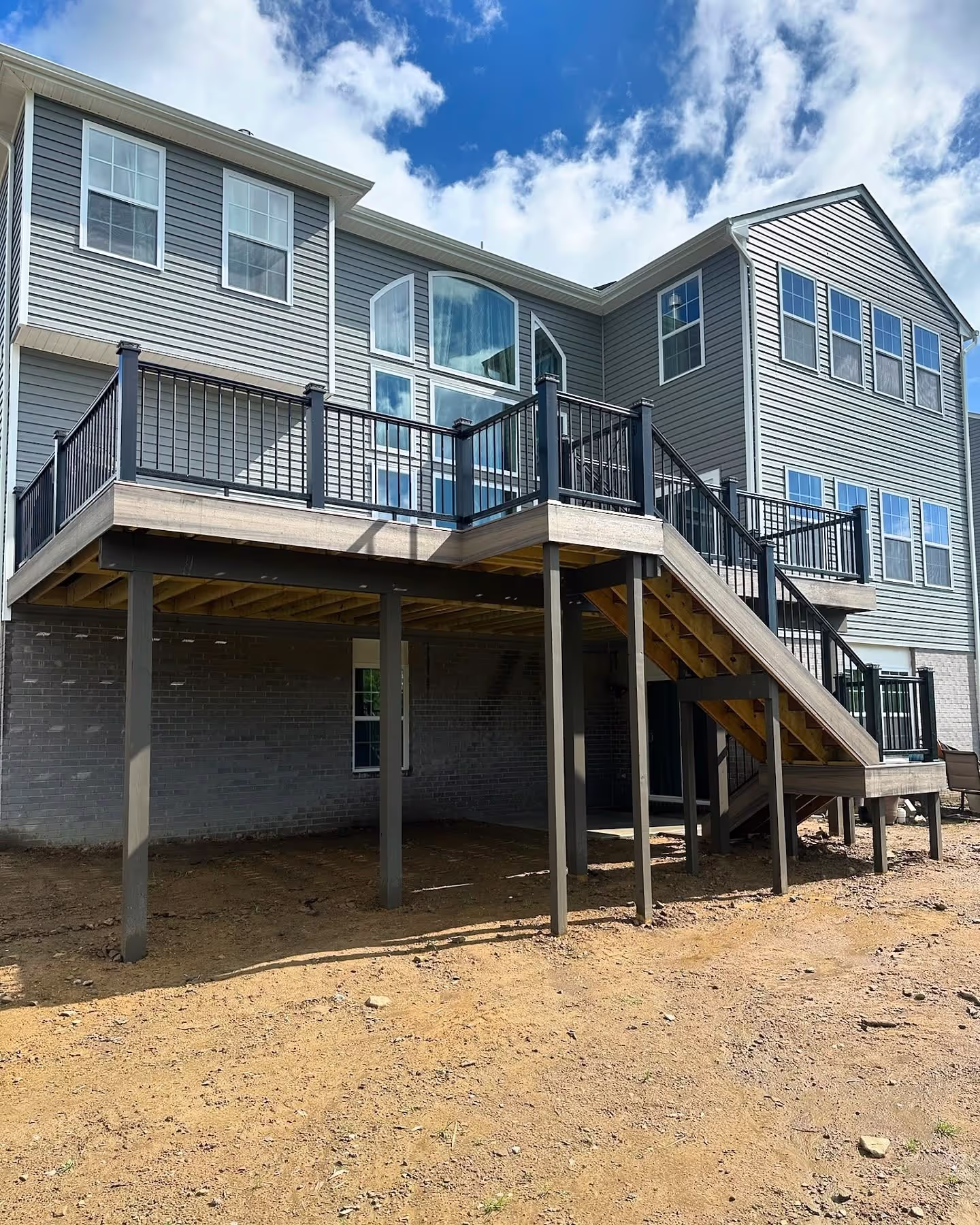 Raised backyard deck with stairs and black aluminum railings on a gray house.