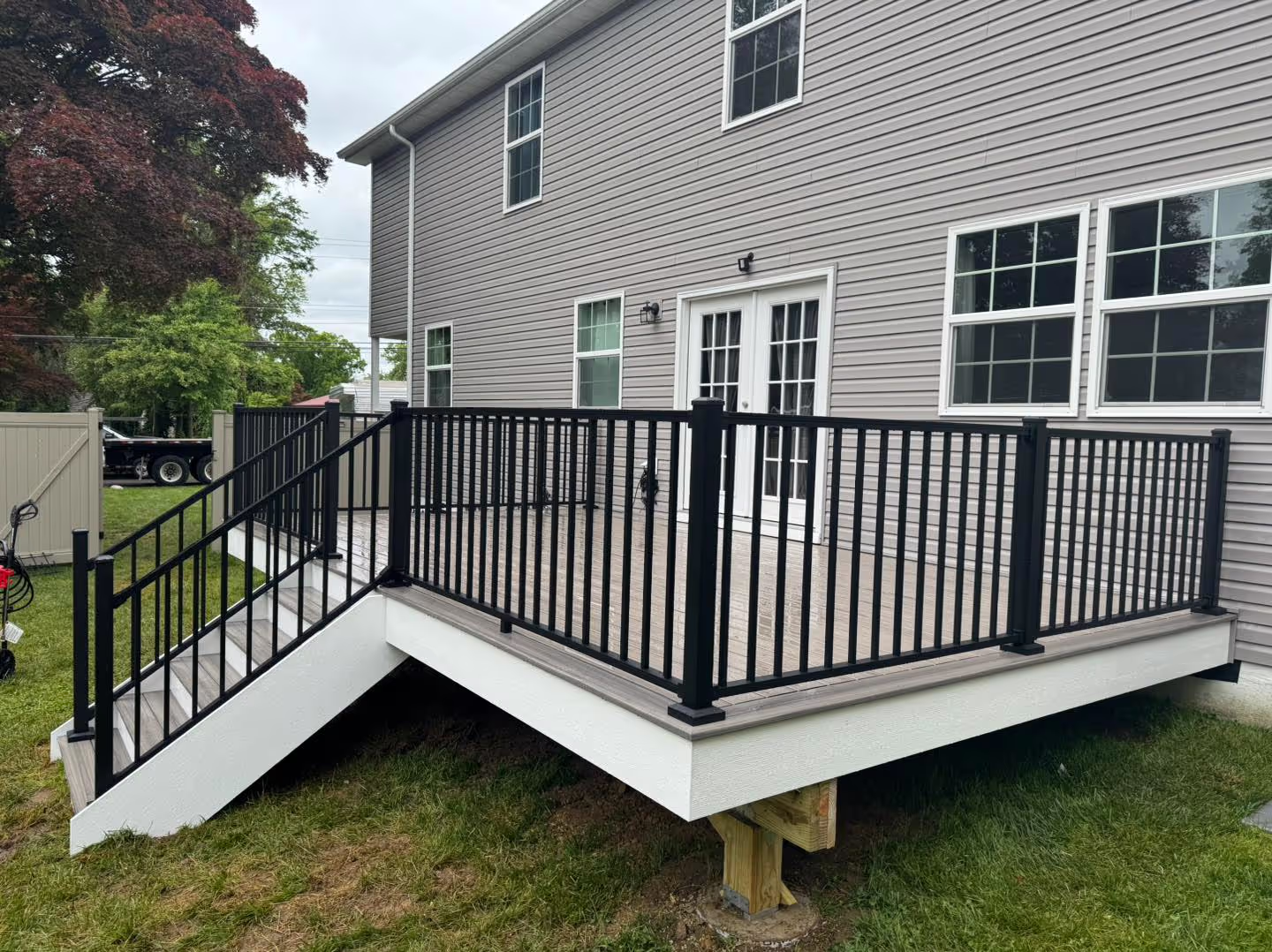 Gray composite deck with black aluminum railings and stairs leading to lawn.