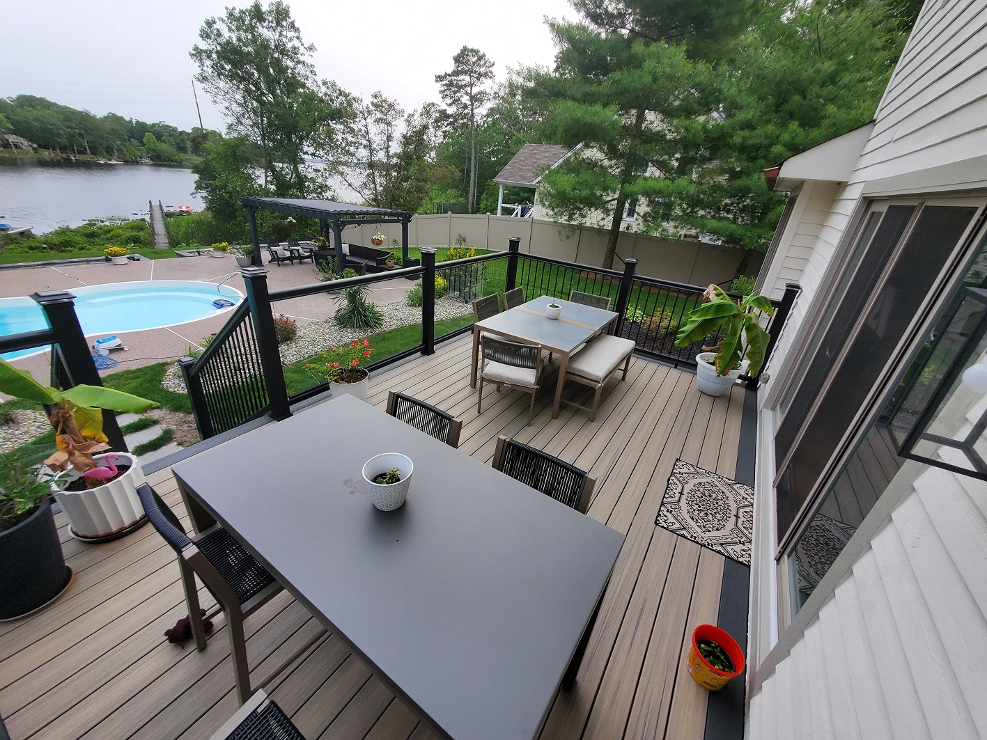 Outdoor deck with dining furniture overlooking a backyard pool and pergola.
