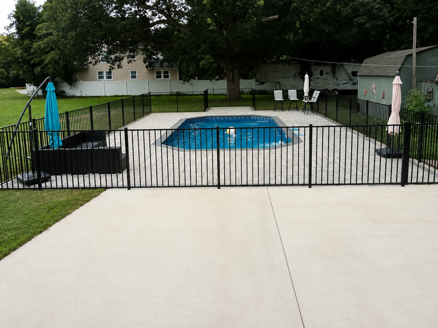 Black aluminum pool safety fence surrounding a backyard pool and patio area.