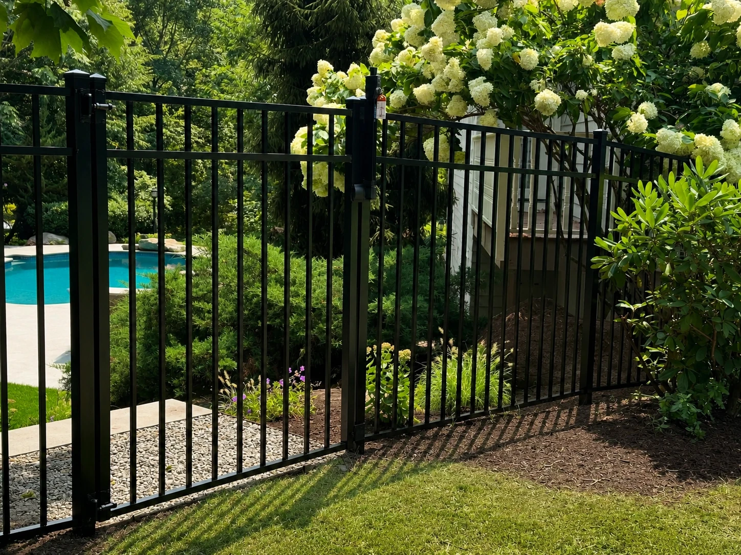Black aluminum fence enclosing a residential yard with mature trees and green lawn.