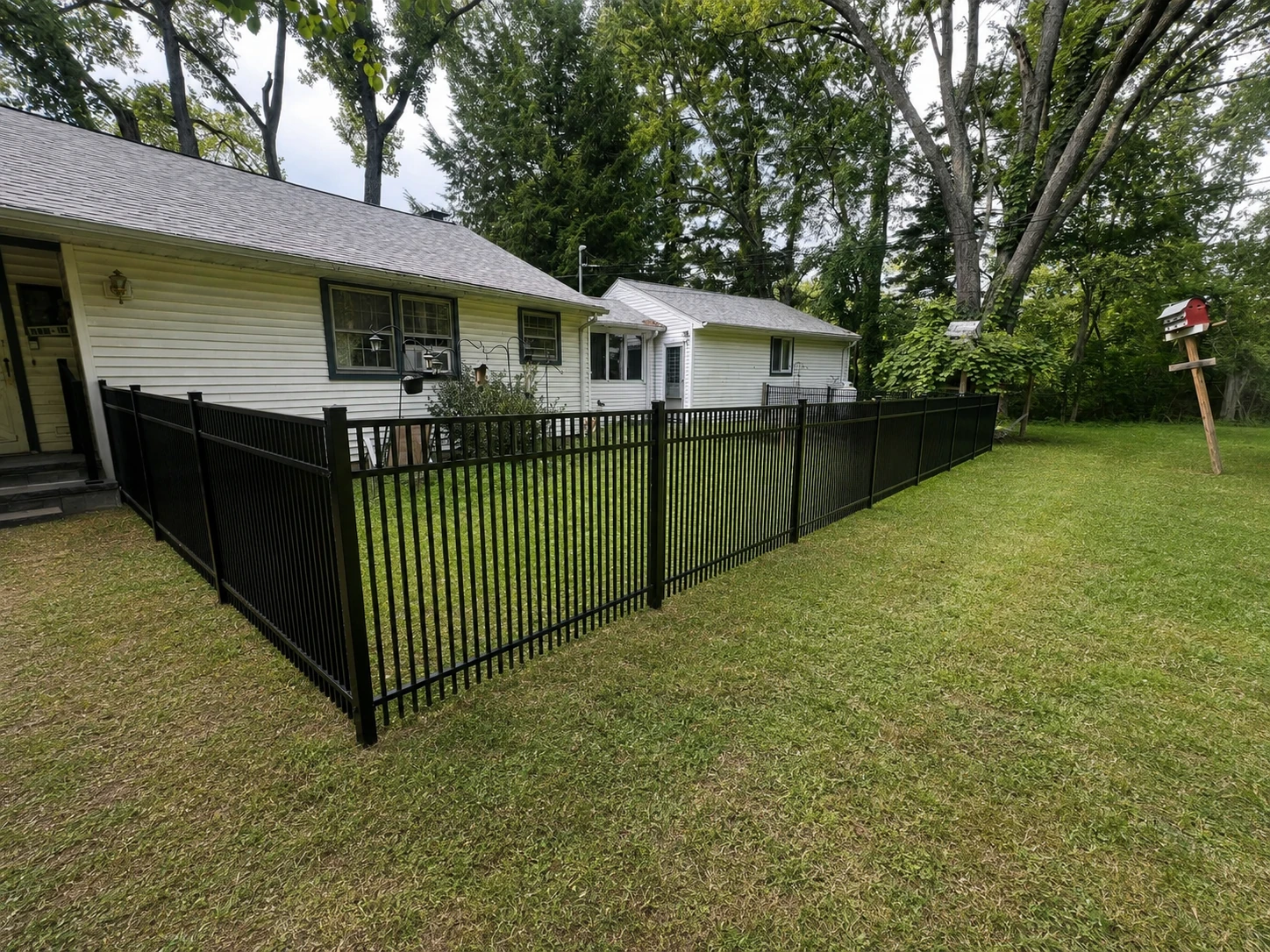 Black aluminum fence enclosing a clean residential backyard beside a white home.