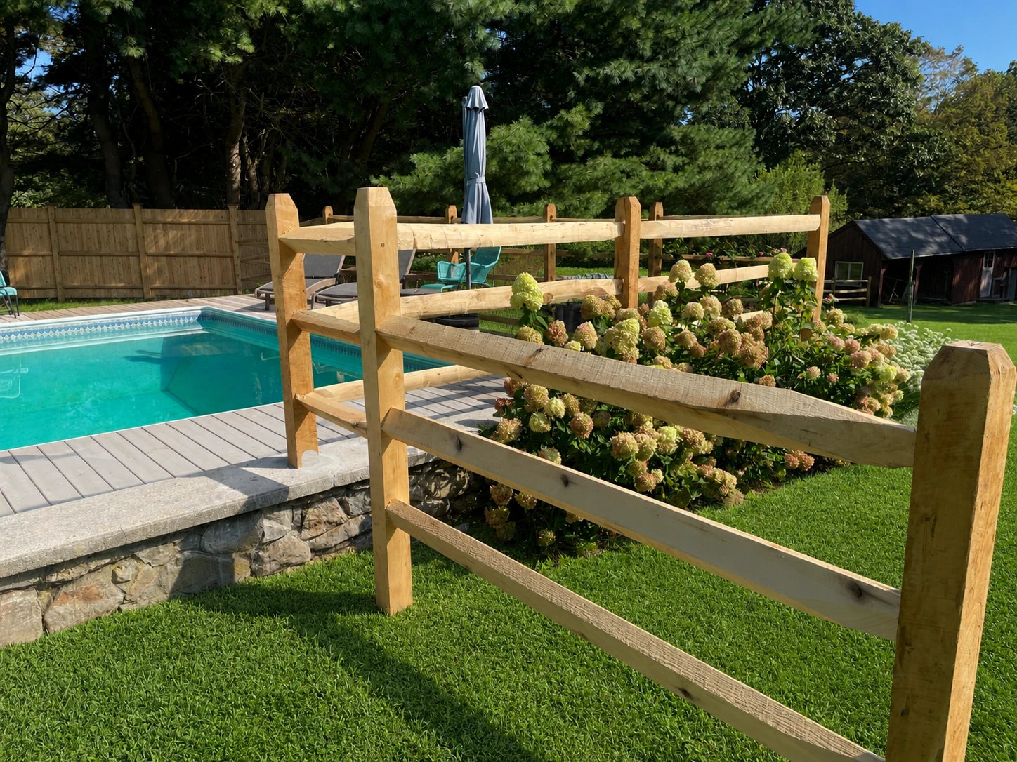 Wood rail fence surrounding an in-ground pool in a landscaped backyard.
