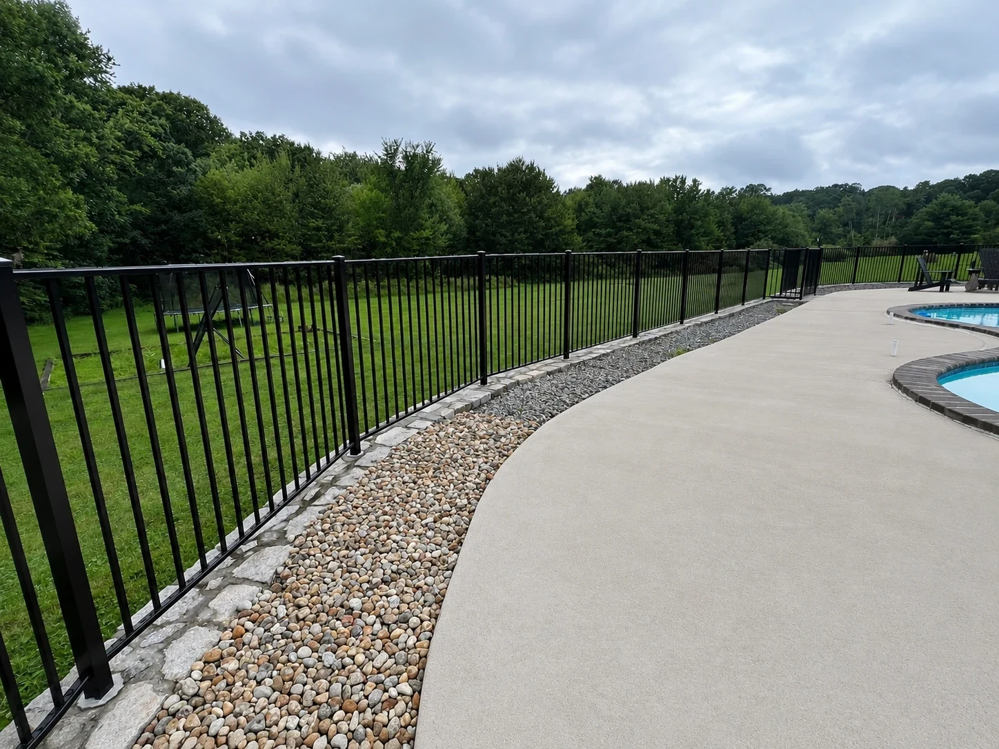 Black aluminum pool fence beside a curved patio and decorative stone border.