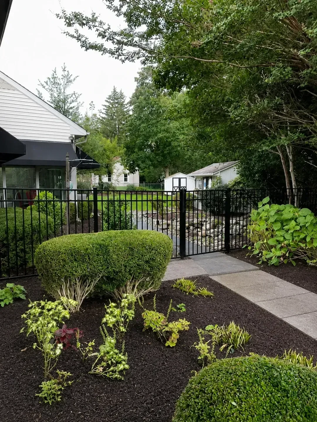 Black aluminum fence with a matching gate in a landscaped residential garden.