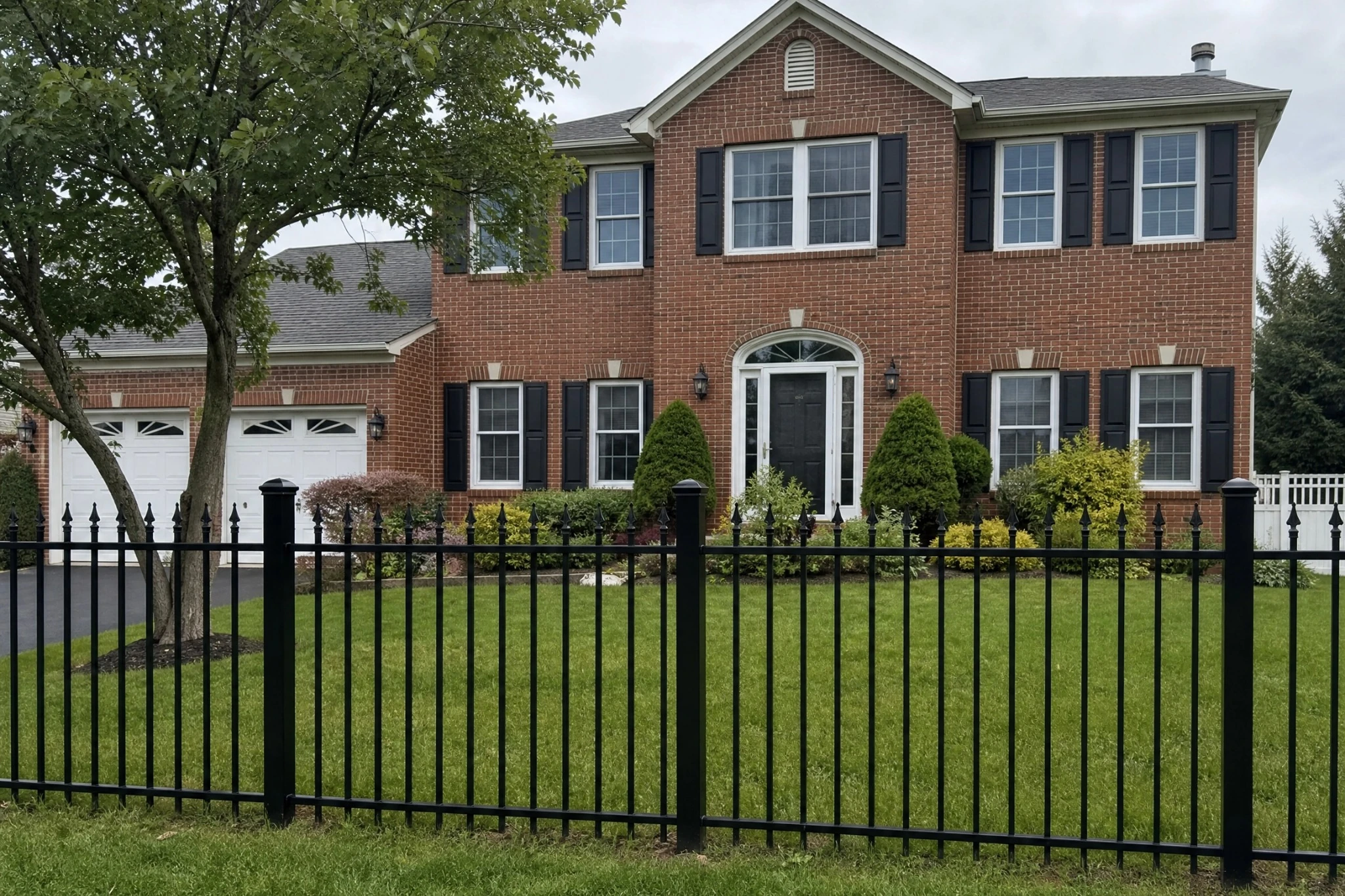Black spear-top ornamental aluminum fence installed across the landscaped front yard of a brick home in Sewell, NJ.