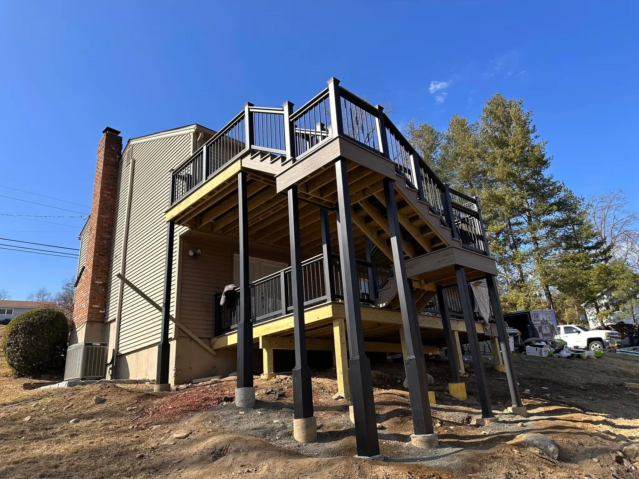 Multi-level raised deck with black railing and stairs under construction by Tri-State Fence & Deck.