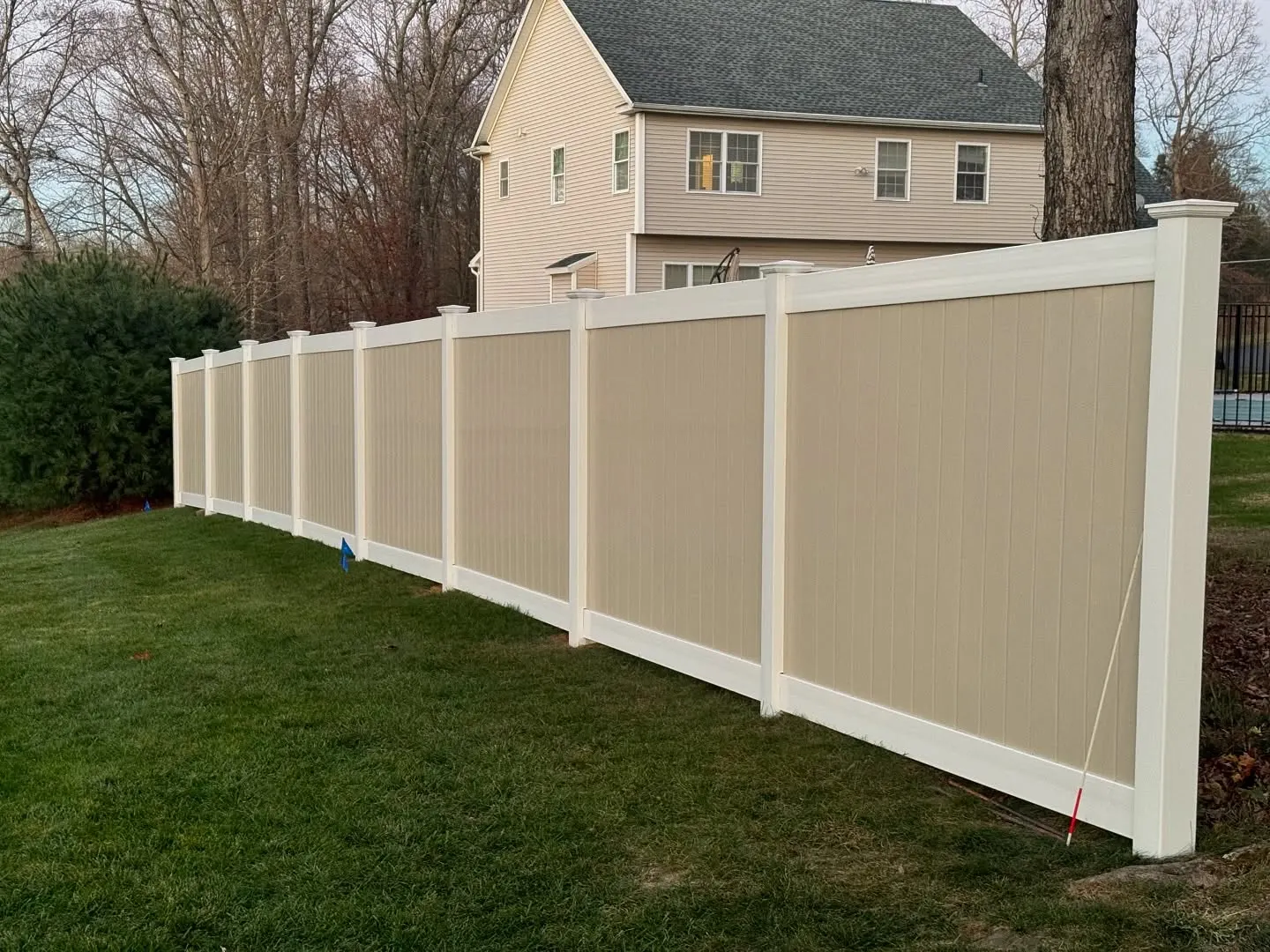 Tan vinyl privacy fence with white posts installed along a residential yard in New Jersey.