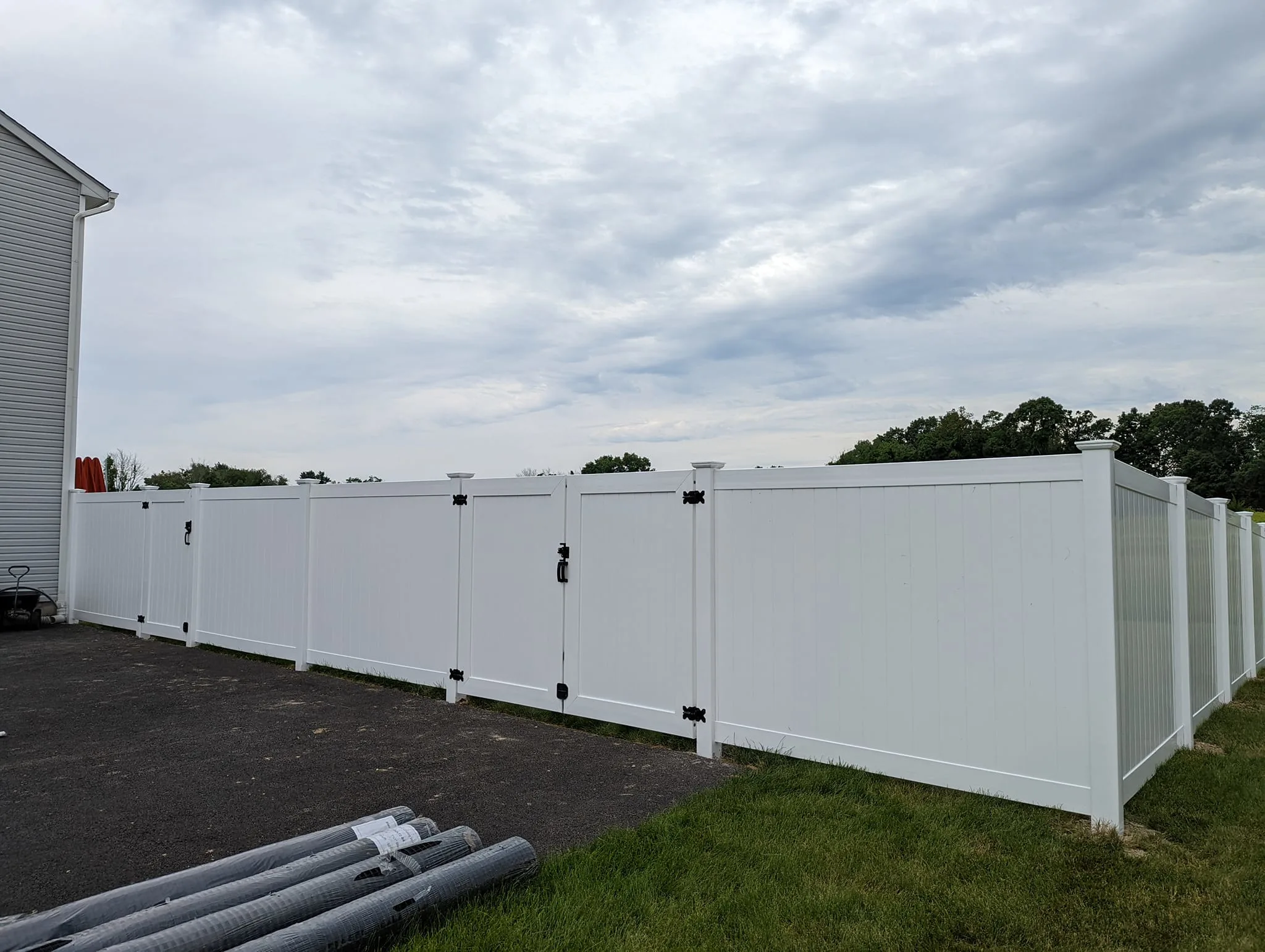 White vinyl privacy fence with double gates and reinforced posts beside a driveway in New Jersey.