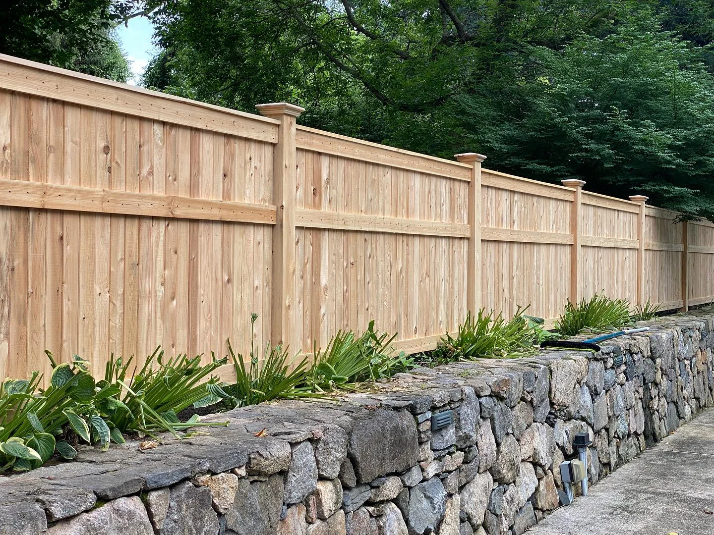 Cedar cap-and-trim privacy fence installed above a stone retaining wall.