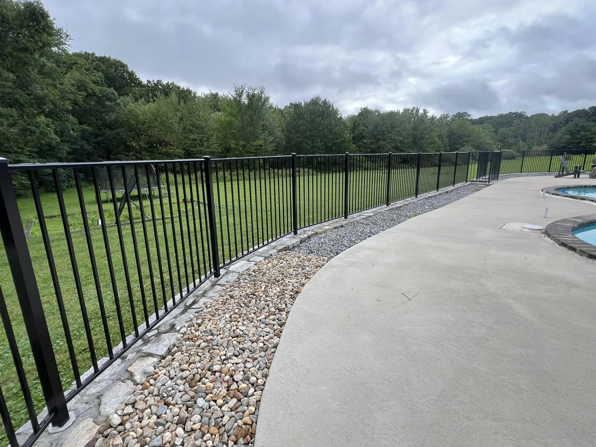Black aluminum pool fence following a curved concrete patio beside a large grassy yard.
