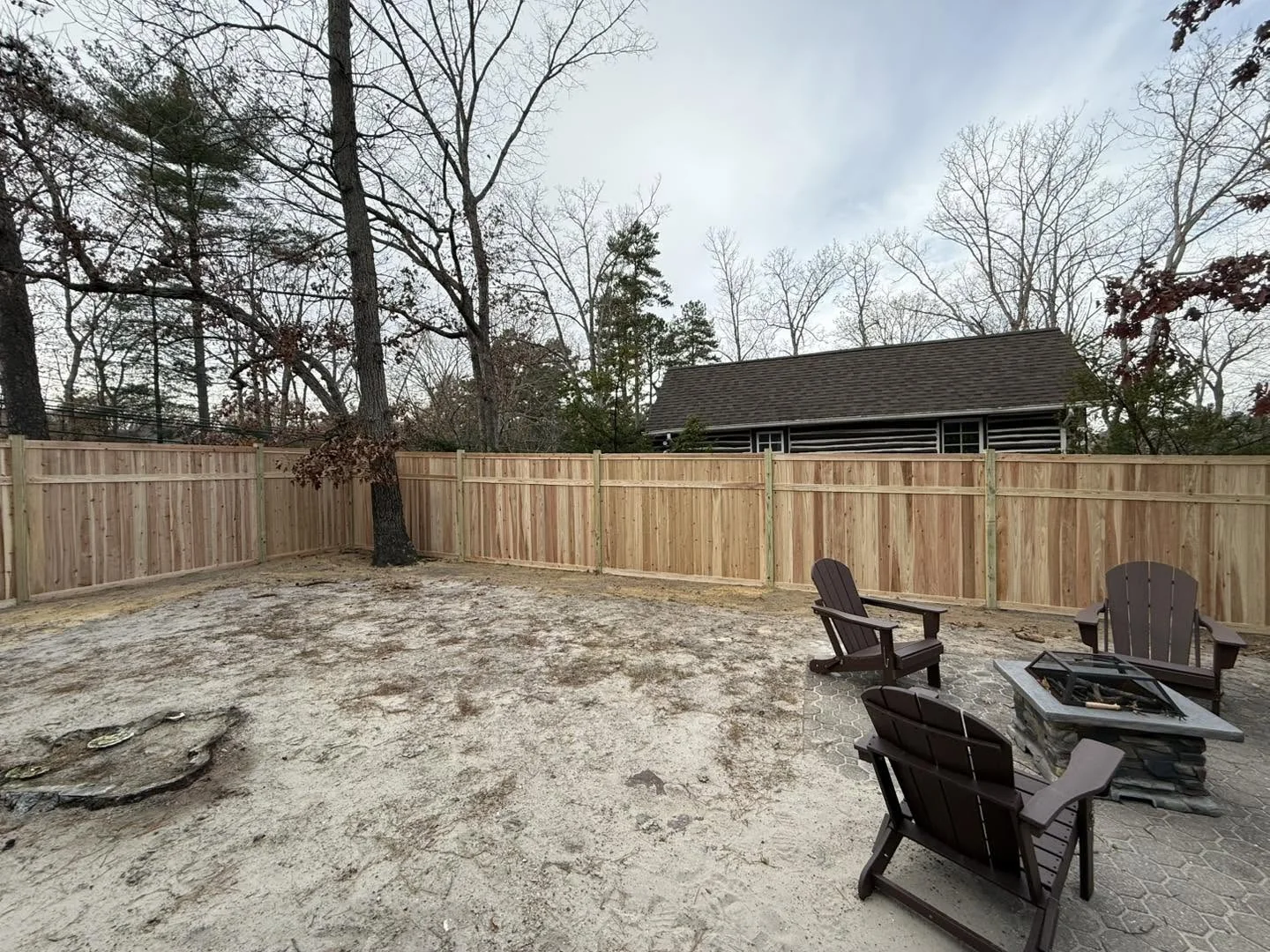 Cedar privacy fence around a sandy backyard patio with Adirondack chairs and a mature tree in Medford Lakes, NJ