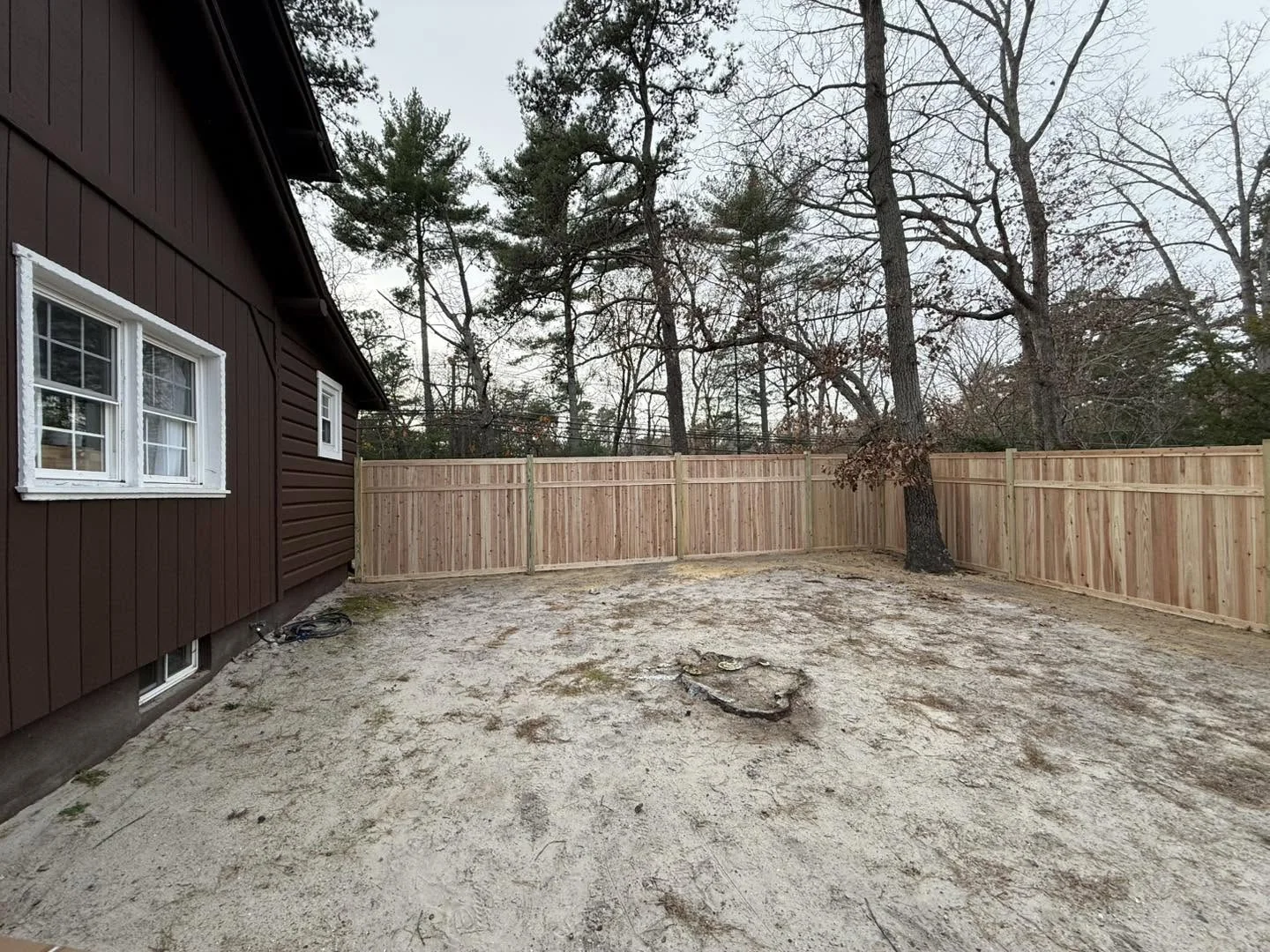 Cedar privacy fence around a sandy backyard patio with Adirondack chairs and a mature tree in Medford Lakes, NJ