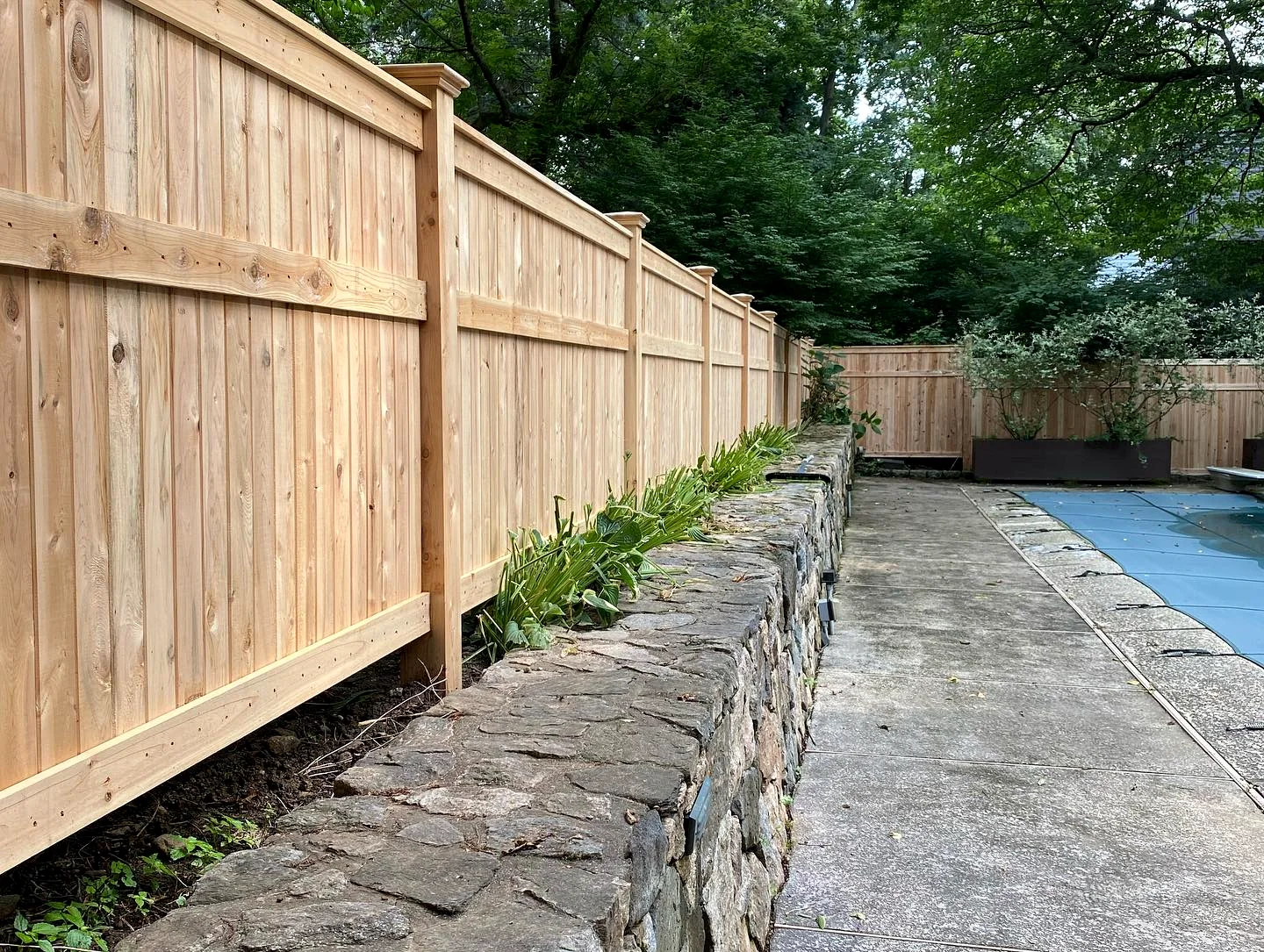 Poolside cedar privacy fence running above a stone retaining wall in Wilmington, DE.