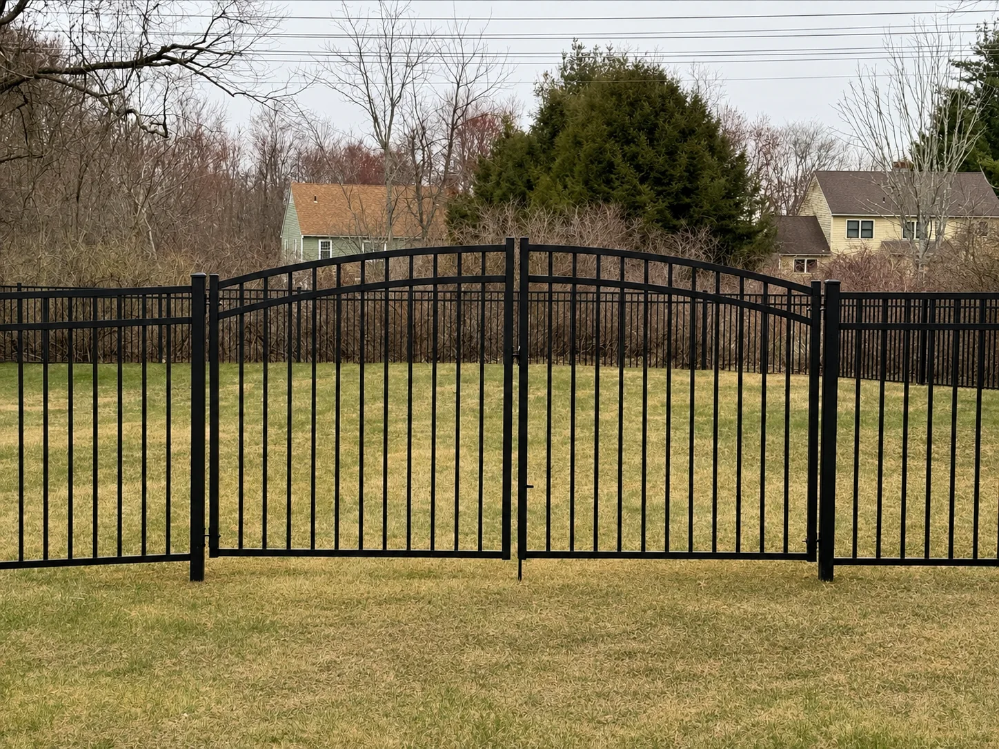Black aluminum double driveway gate with arched rails in a residential yard.