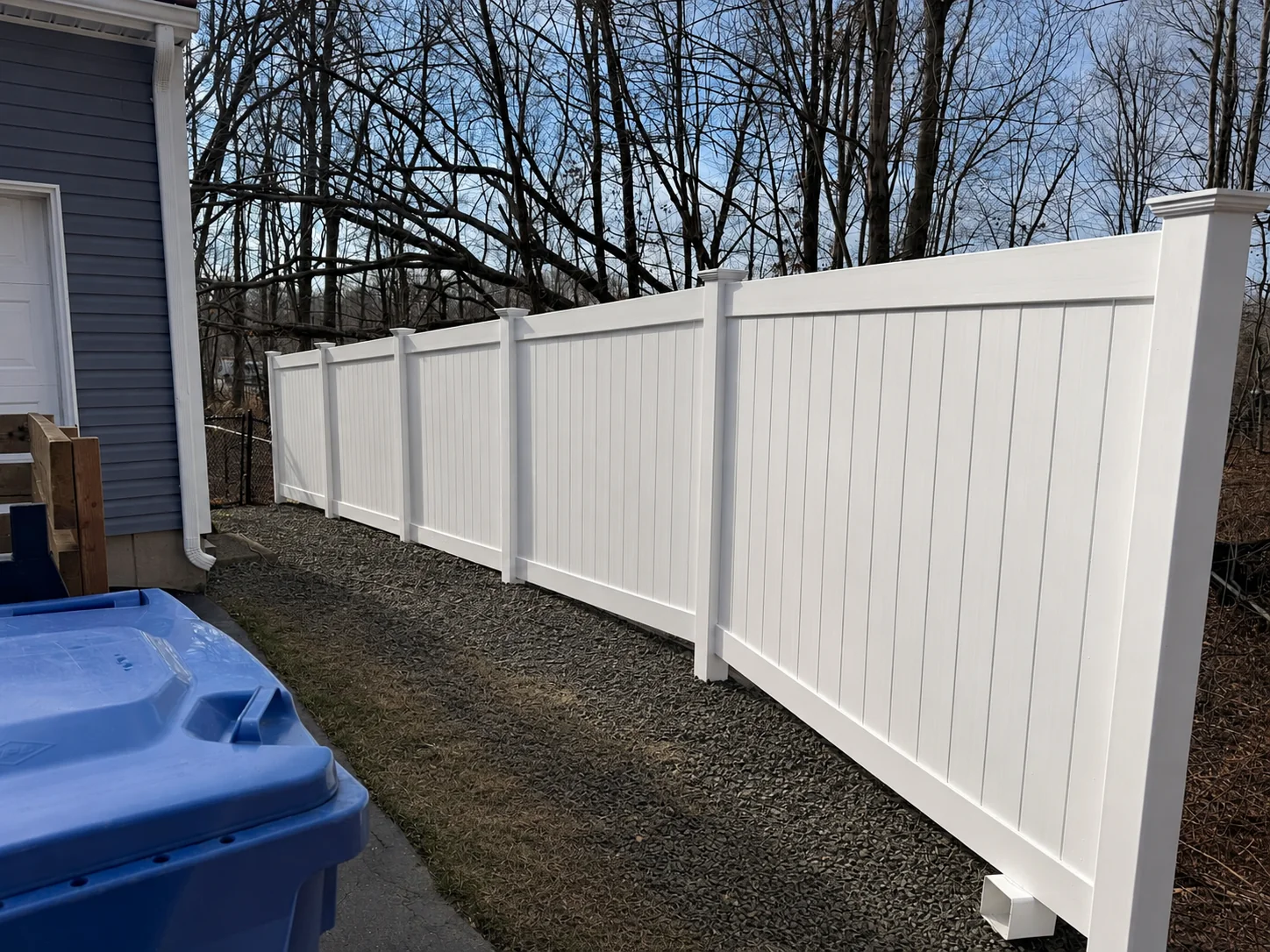White vinyl privacy fence installed beside a home and wooded property line.