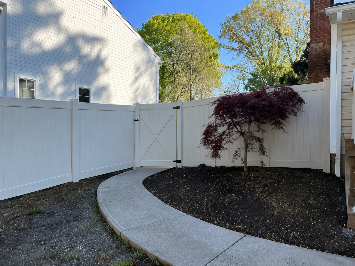 White vinyl privacy fence with gate beside a curved walkway in Harrison Township, NJ.