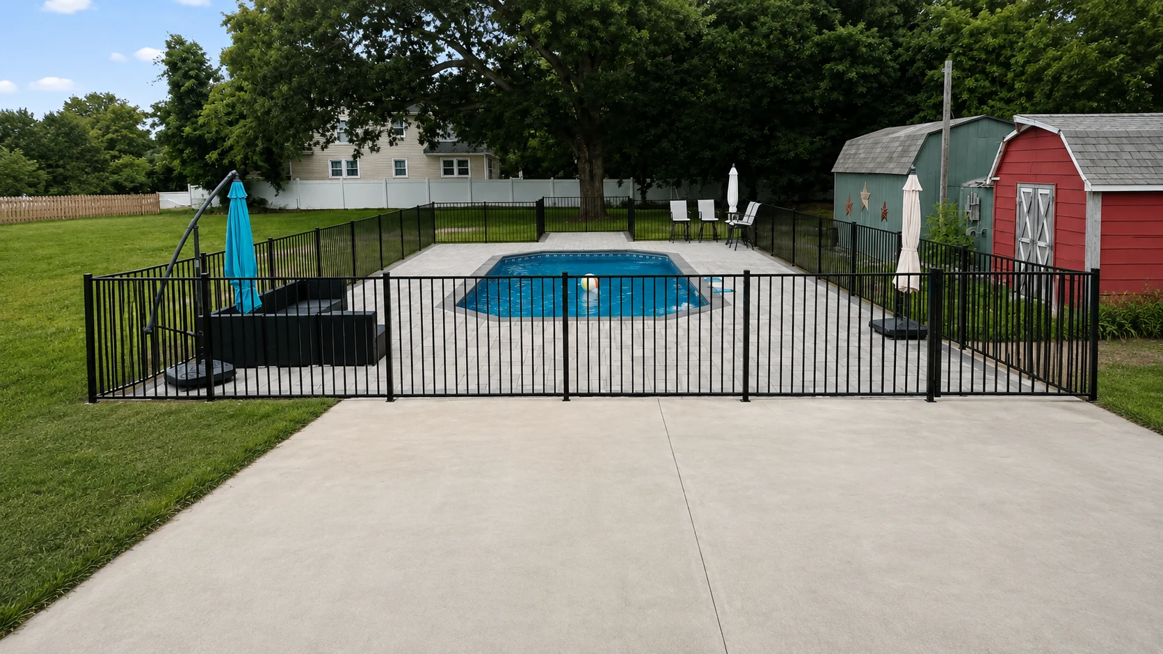 Black aluminum safety fence surrounding an in-ground backyard swimming pool and patio.