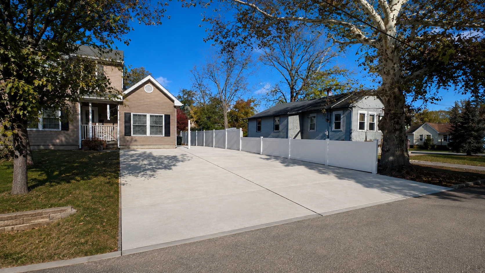 White vinyl fence running alongside a wide residential driveway between neighboring homes.