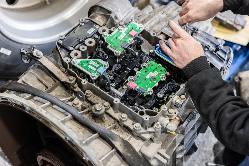 Transmission repair with technicians servicing a heavy-duty automatic transmission valve body and electronic control modules.