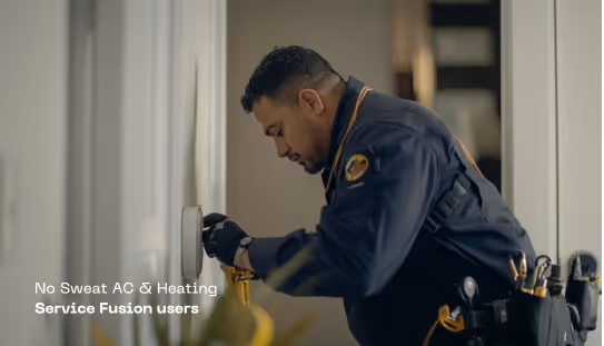 Technician in blue uniform adjusting a thermostat on a wall inside a home.